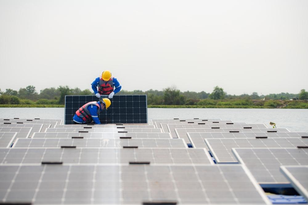Two people in hard hats and hi vis work wear at work installing solar panels in the middle of a solar panel field.